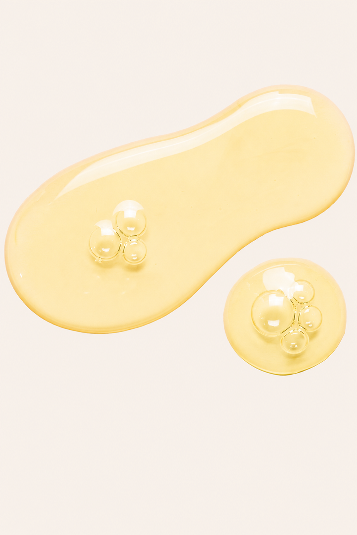 A glossy, translucent yellow cosmetic or skincare serum droplet with small bubbles on a solid off-white background.