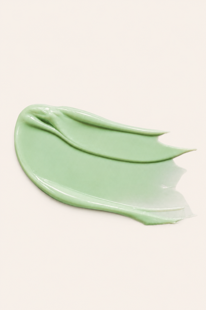 A thick, smooth smear of light mint green cosmetic cream or gel on a solid, warm off-white background.