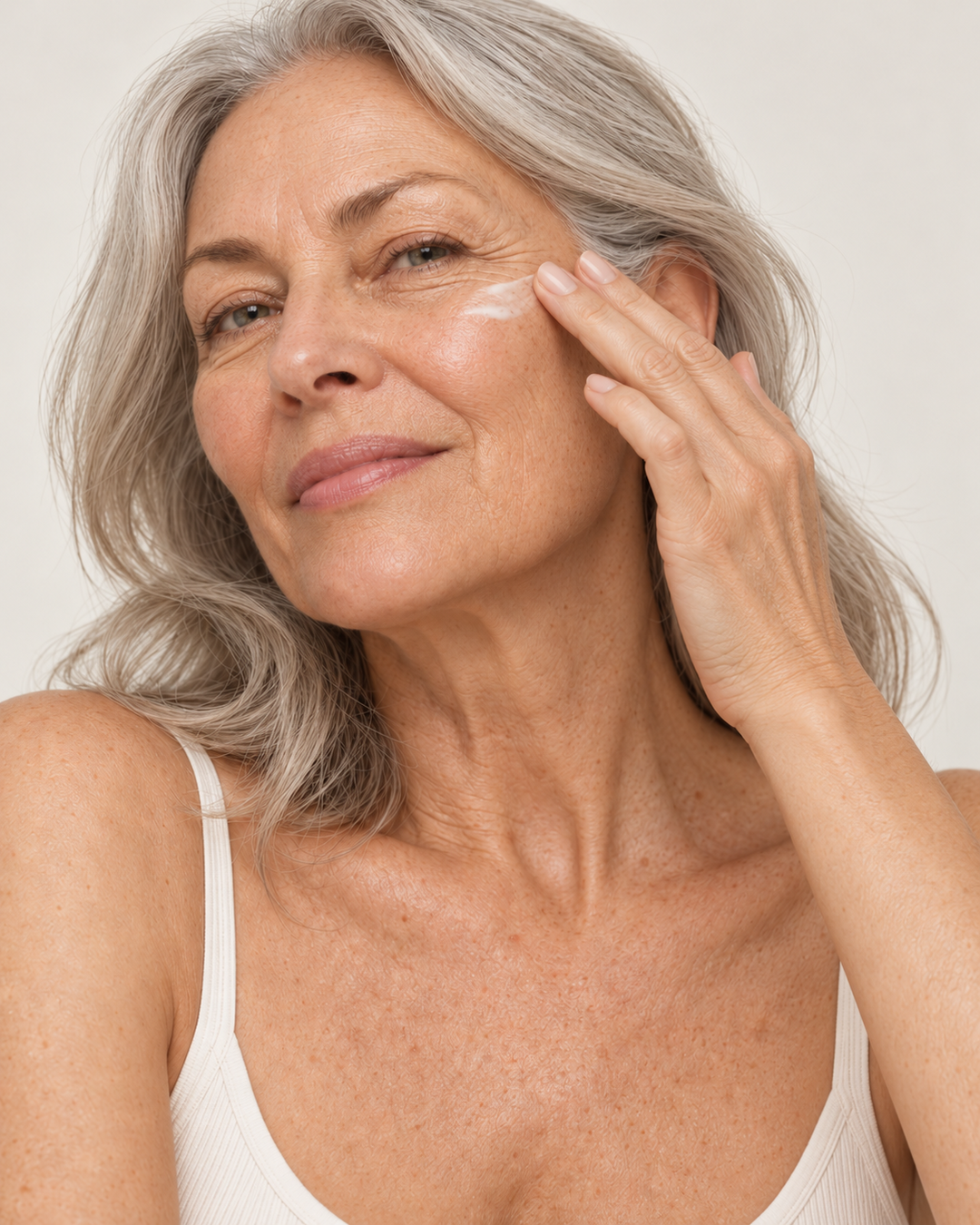 NAYA mature silver-haired model with natural skin texture gently applying white face cream