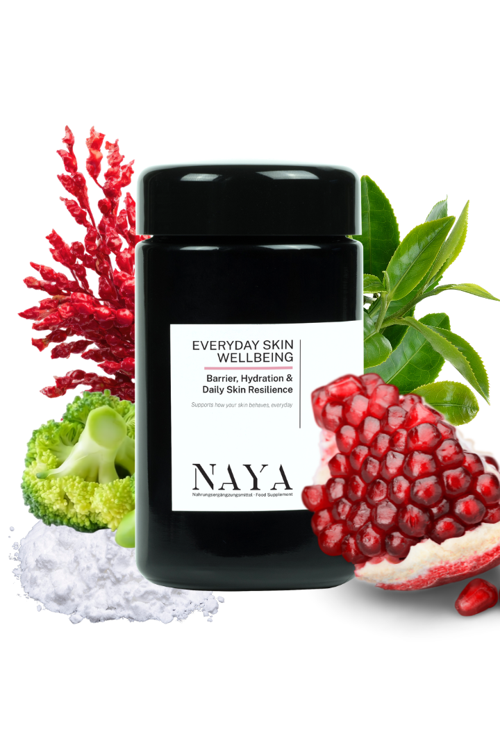 A black cosmetic jar labeled 'EVERYDAY SKIN WELLBEING' by NAYA, surrounded by natural ingredients including broccoli, red coral, pomegranate, green leaves, and a pile of white powder on a white background.